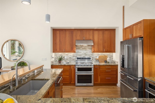 kitchen featuring appliances with stainless steel finishes, brown cabinetry, a sink, and under cabinet range hood