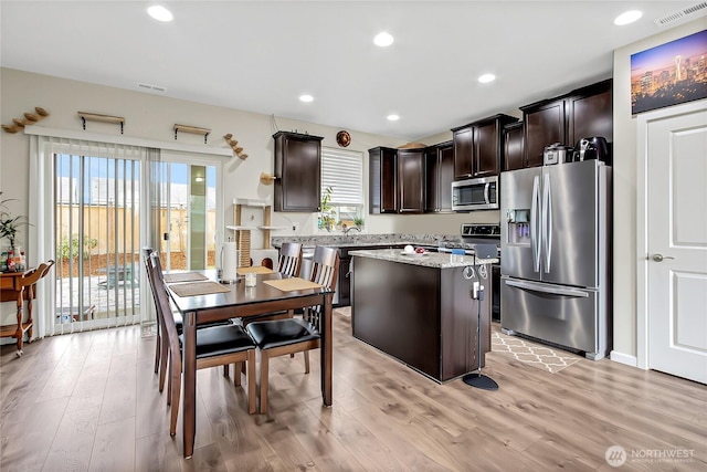 kitchen featuring visible vents, light wood-style flooring, a kitchen island, appliances with stainless steel finishes, and dark brown cabinets