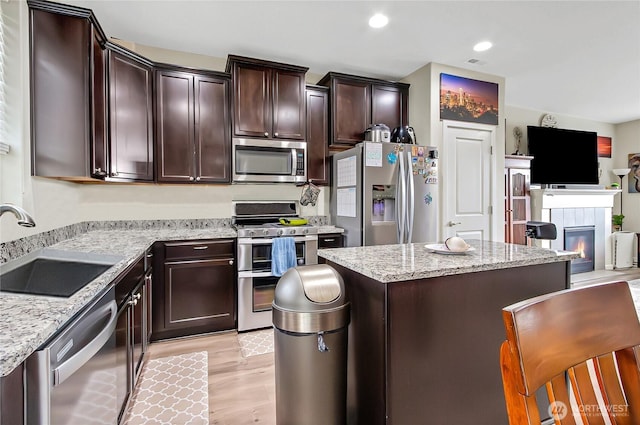 kitchen with a tile fireplace, stainless steel appliances, a kitchen island, a sink, and dark brown cabinets