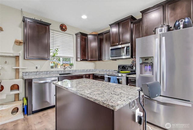 kitchen featuring dark brown cabinetry, light stone countertops, stainless steel appliances, a center island, and light wood finished floors