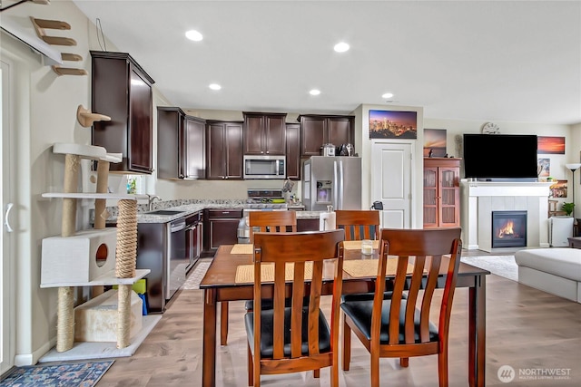 kitchen featuring stainless steel appliances, recessed lighting, open floor plan, dark brown cabinetry, and a tile fireplace