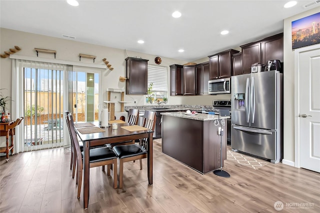 kitchen featuring a center island, light wood-style floors, dark brown cabinets, appliances with stainless steel finishes, and light stone countertops