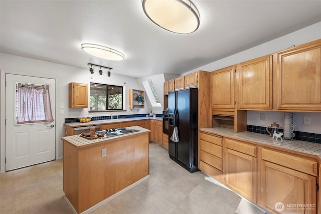 kitchen with tile counters, appliances with stainless steel finishes, a center island, light floors, and a sink