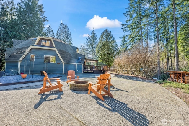 rear view of house with a fire pit, a deck, and roof with shingles