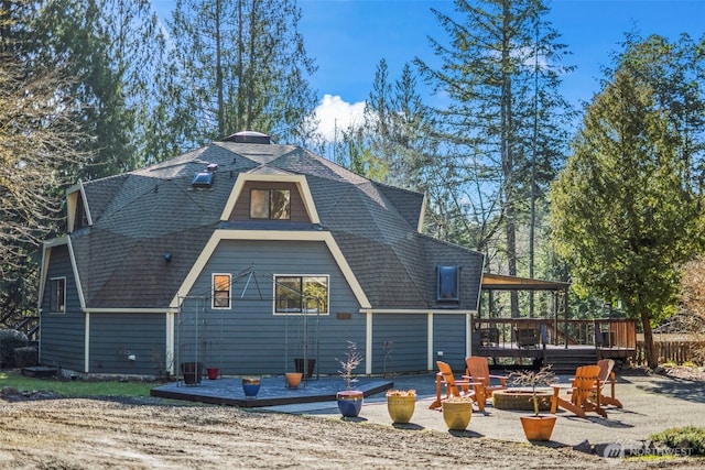 back of property with a shingled roof, an outdoor fire pit, a patio area, and a wooden deck