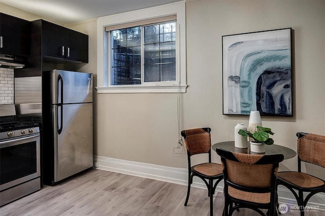 kitchen with dark cabinets, baseboards, appliances with stainless steel finishes, range hood, and light wood finished floors