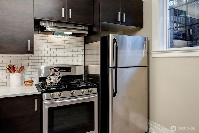 kitchen with under cabinet range hood, appliances with stainless steel finishes, dark brown cabinets, and backsplash