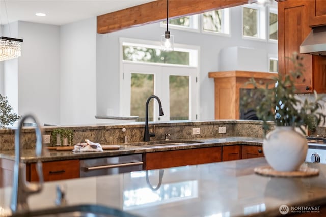 kitchen with brown cabinets, pendant lighting, a sink, dark stone countertops, and stainless steel dishwasher