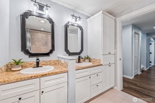 full bath featuring backsplash, two vanities, baseboards, and a sink