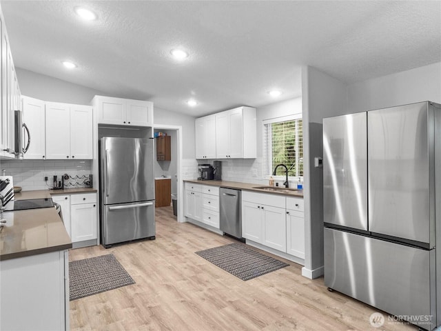 kitchen featuring light wood-style flooring, stainless steel appliances, a sink, white cabinetry, and vaulted ceiling