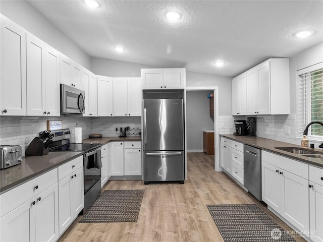 kitchen featuring dark countertops, vaulted ceiling, stainless steel appliances, light wood-style floors, and a sink