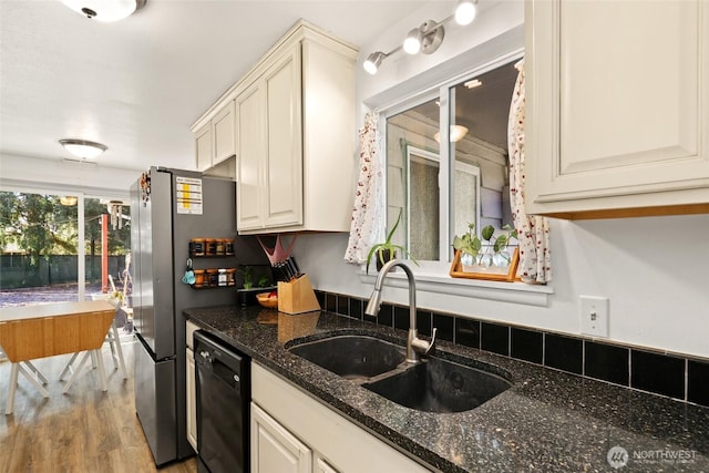 kitchen with dark stone counters, wood finished floors, a sink, freestanding refrigerator, and dishwasher