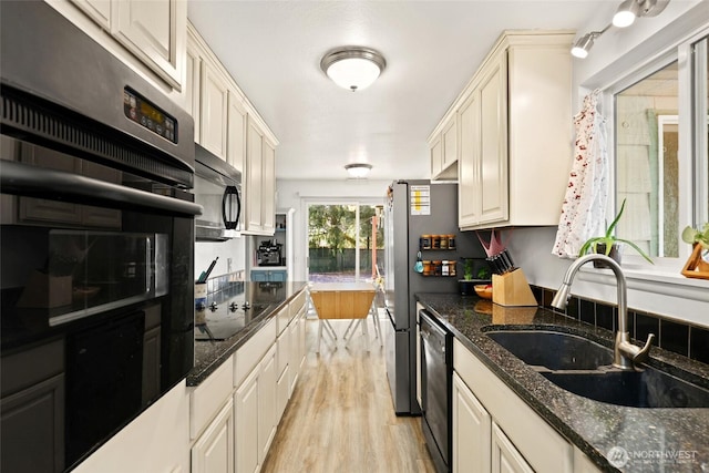 kitchen featuring dark stone countertops, a sink, light wood-style flooring, and black appliances