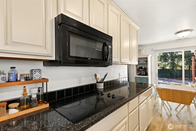 kitchen featuring dark stone counters, black appliances, and light wood finished floors