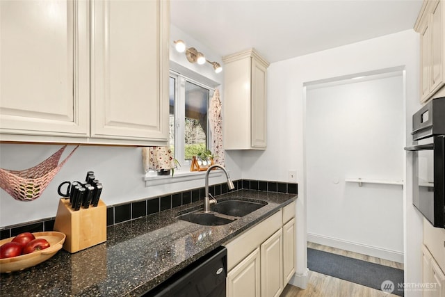 kitchen with black dishwasher, dark stone counters, stainless steel oven, a sink, and light wood-type flooring