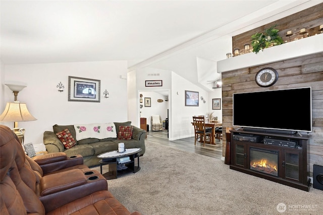 living room with a glass covered fireplace, lofted ceiling, carpet flooring, and visible vents