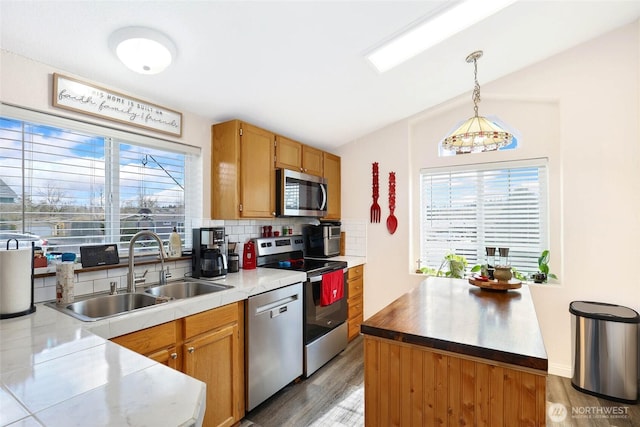 kitchen featuring light wood-style flooring, a sink, hanging light fixtures, stainless steel appliances, and backsplash