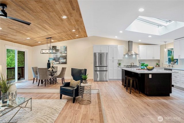 kitchen with stainless steel appliances, light countertops, a kitchen island, vaulted ceiling with skylight, and wall chimney exhaust hood