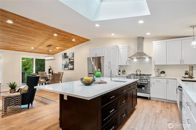 kitchen featuring wall chimney range hood, appliances with stainless steel finishes, white cabinets, and a sink