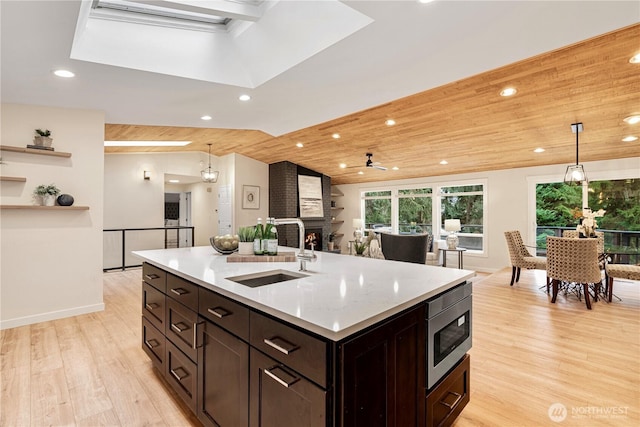 kitchen featuring light wood-style floors, a fireplace, stainless steel microwave, and a sink