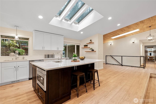 kitchen with a center island with sink, visible vents, lofted ceiling with skylight, light countertops, and a sink