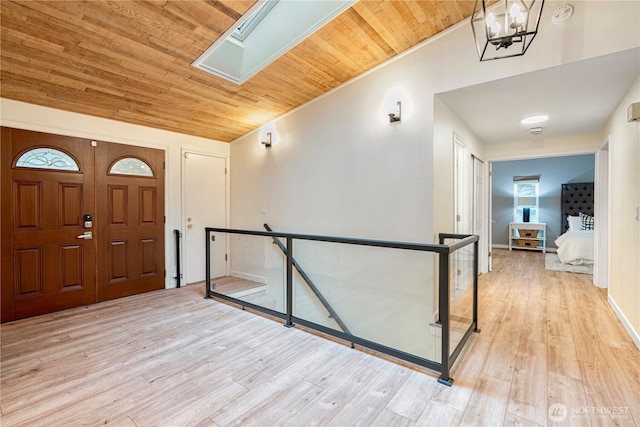 entryway featuring an inviting chandelier, light wood-type flooring, wooden ceiling, vaulted ceiling with skylight, and baseboards