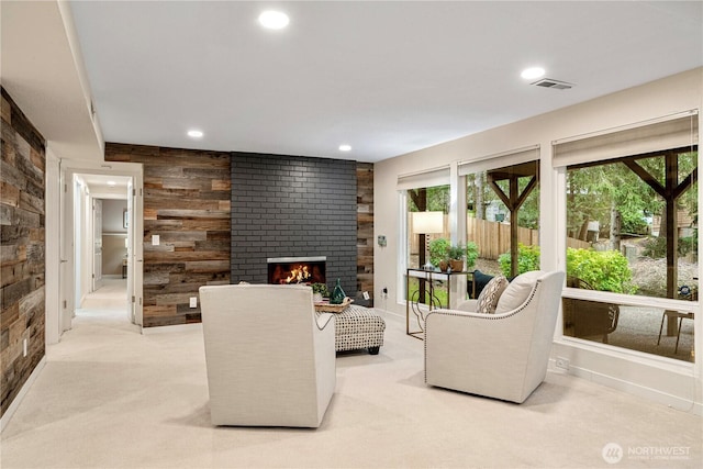 living room with visible vents, light colored carpet, wood walls, a brick fireplace, and recessed lighting