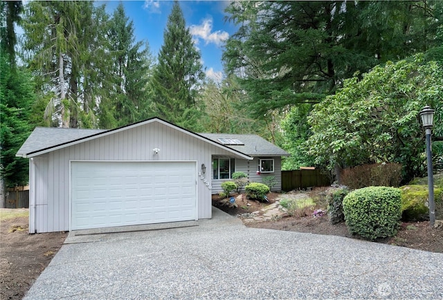 ranch-style house featuring driveway, an attached garage, roof mounted solar panels, and fence