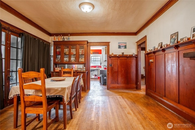 dining area with a textured ceiling, ornamental molding, and light wood-style floors