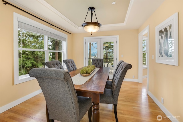 dining room with a tray ceiling, baseboards, light wood-style flooring, and crown molding