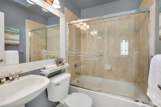 full bath featuring toilet, combined bath / shower with glass door, and a sink