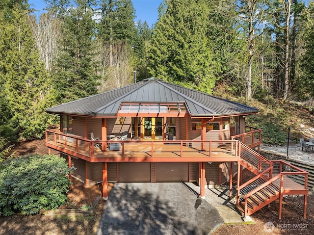 back of property with metal roof, a view of trees, a garage, driveway, and a standing seam roof