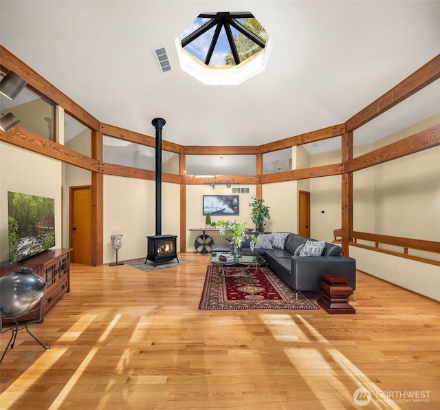 living area with visible vents, a skylight, a wood stove, wood finished floors, and high vaulted ceiling