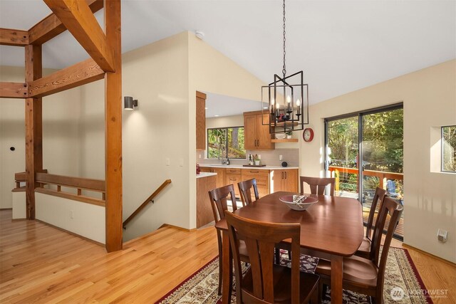 dining room with light wood-type flooring, an inviting chandelier, and vaulted ceiling