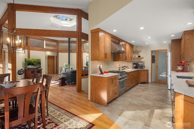 kitchen with light countertops, decorative backsplash, high end appliances, wall chimney exhaust hood, and a sink