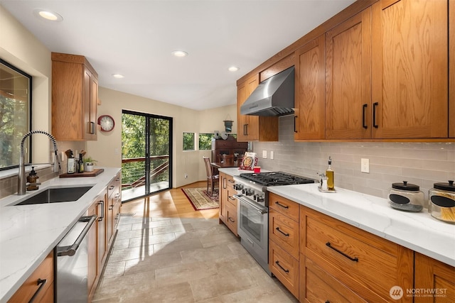 kitchen featuring a sink, stainless steel appliances, brown cabinetry, and wall chimney range hood