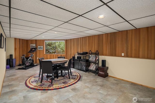 dining area featuring a drop ceiling, baseboards, and wood walls