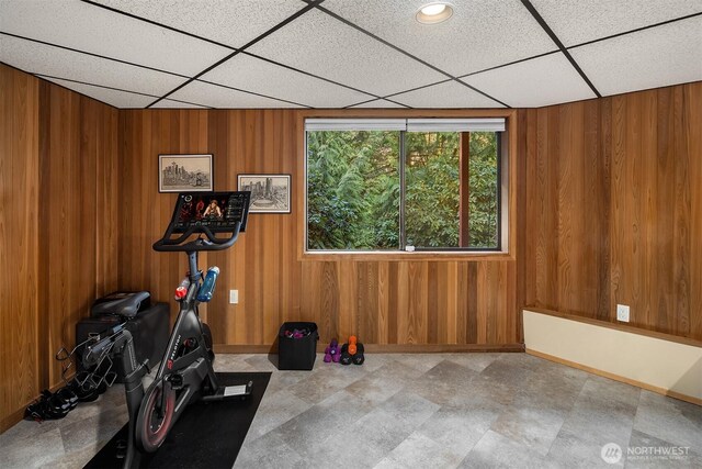 exercise area with tile patterned floors, wooden walls, a paneled ceiling, and baseboards