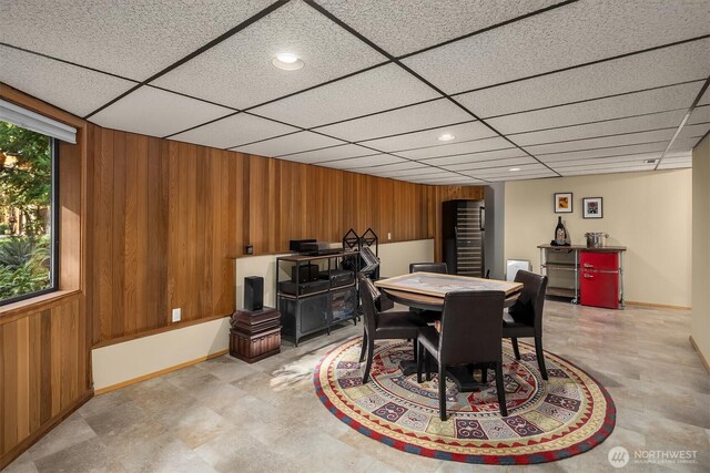 dining area with baseboards, a drop ceiling, wood walls, light floors, and recessed lighting