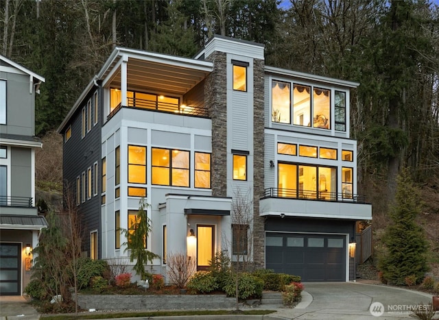 contemporary house with stone siding, an attached garage, and concrete driveway