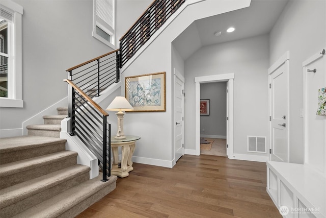 staircase featuring recessed lighting, visible vents, a towering ceiling, wood finished floors, and baseboards