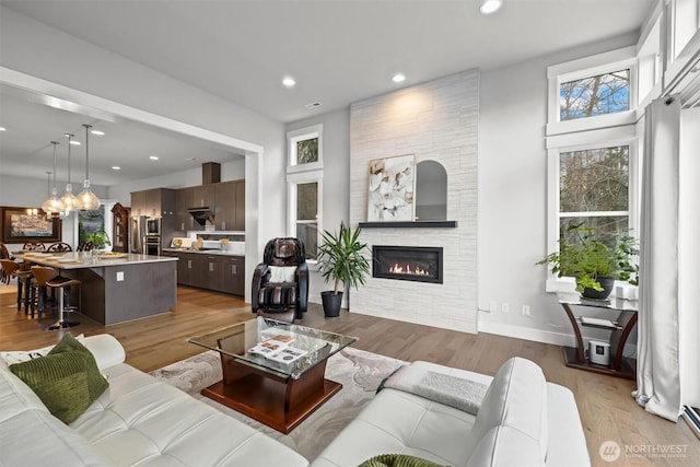 living room featuring recessed lighting, a fireplace, light wood-style flooring, and baseboards