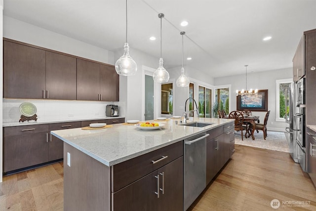 kitchen with dark brown cabinetry, a center island with sink, dishwasher, light wood-type flooring, and a sink