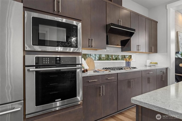 kitchen with appliances with stainless steel finishes, light wood-type flooring, backsplash, and dark brown cabinetry