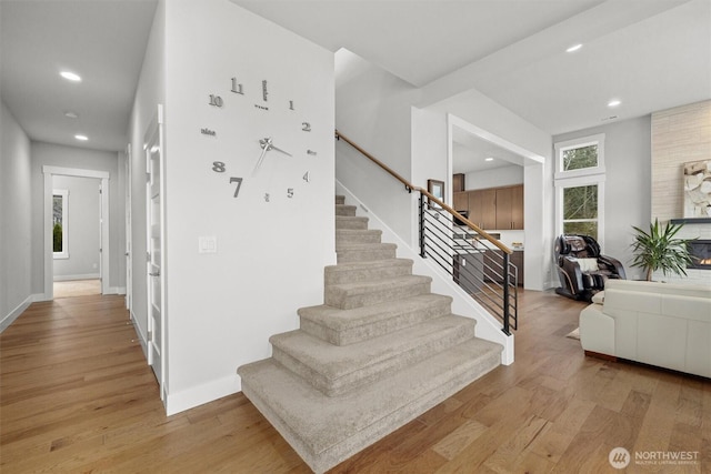 stairway featuring baseboards, a large fireplace, wood finished floors, and recessed lighting