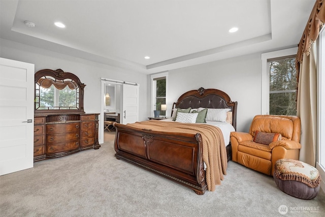 carpeted bedroom with a barn door, a raised ceiling, connected bathroom, and recessed lighting