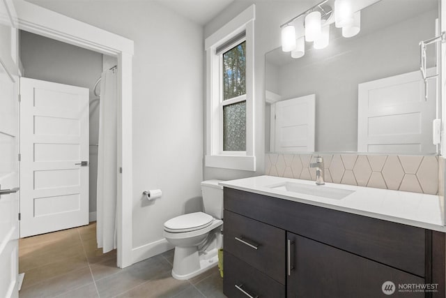 bathroom featuring tile patterned flooring, toilet, vanity, baseboards, and tasteful backsplash