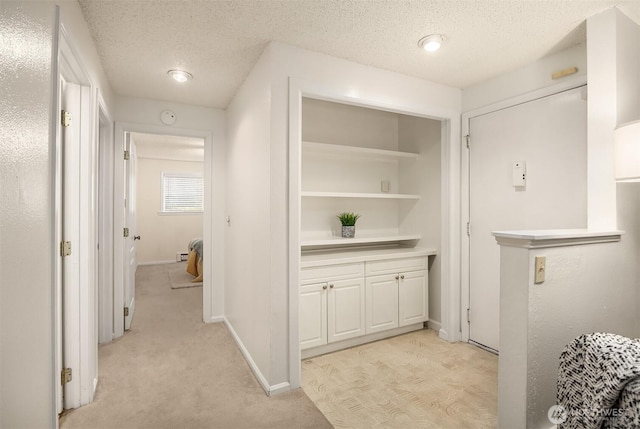 hallway with a textured ceiling, light colored carpet, and baseboards