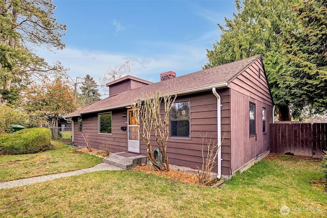 view of front of home with roof with shingles, a chimney, a front yard, and fence