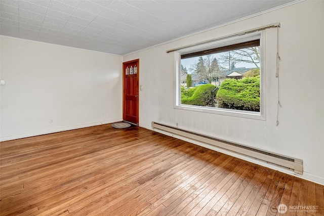 empty room featuring a baseboard heating unit, baseboards, and wood-type flooring